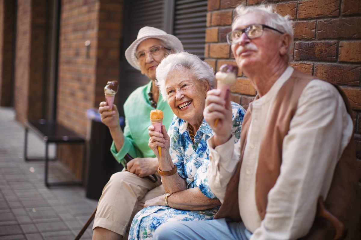 portrait-of-three-senior-friends-eating-ice-cream A senior couple sitting in a chair laughing with friends